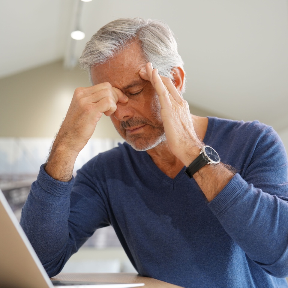 Senior man having a headache while working on laptop computer