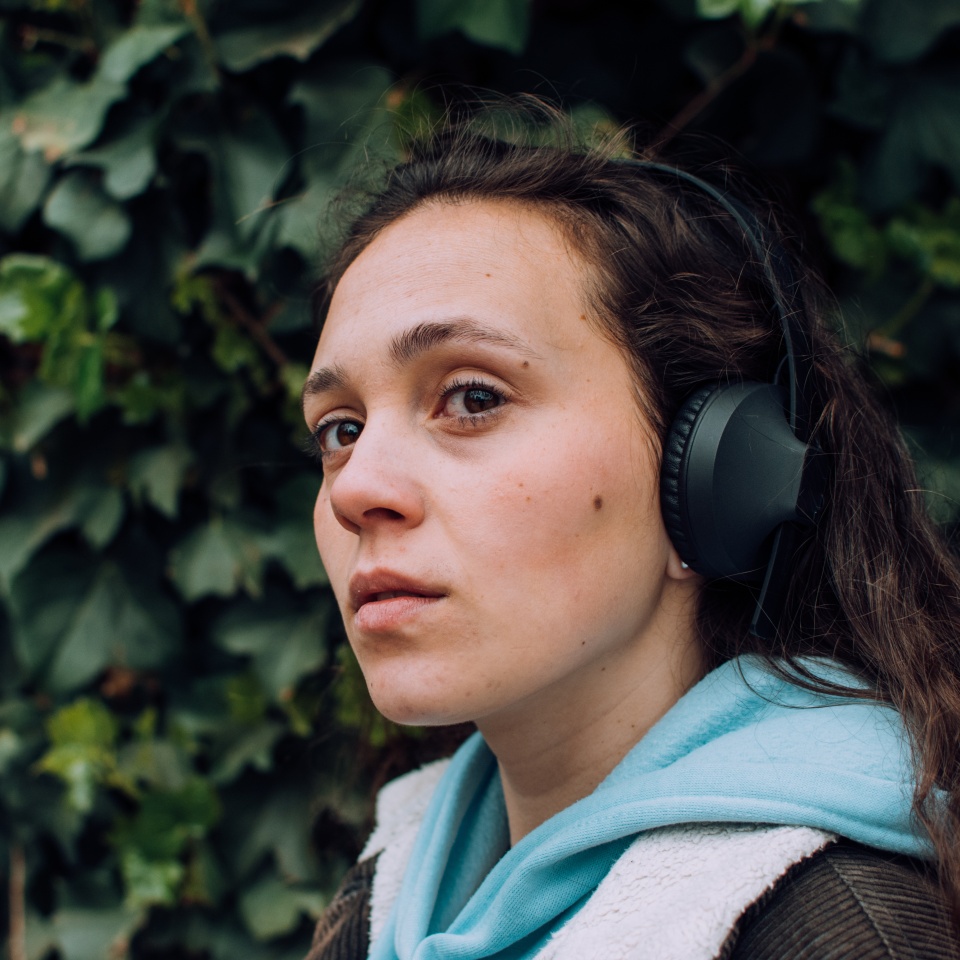 Young girl listening to music with her headphones in the open air, park, street. Outdoor. Green background, natural, grass. Young model profile. Neutral face.