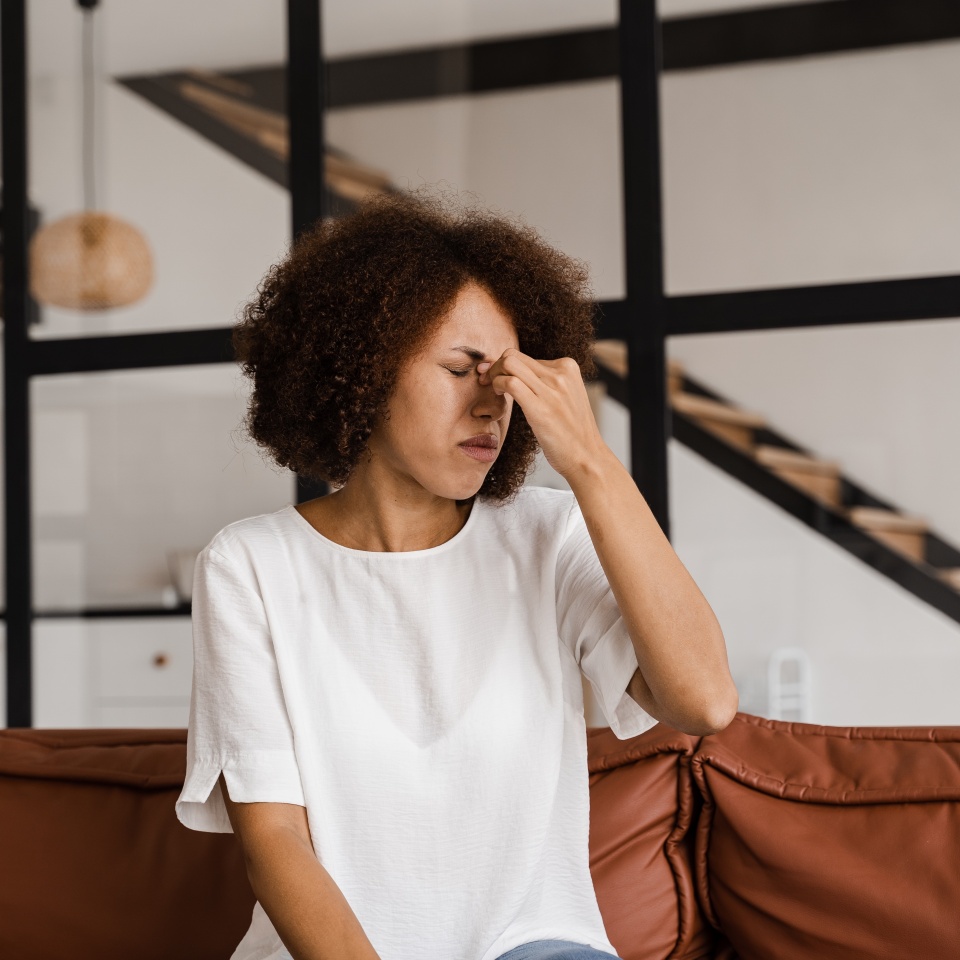 Sick African girl with sinusitis is holding her stuffy nose because she has rhinitis and is planning to go to the ENT doctor