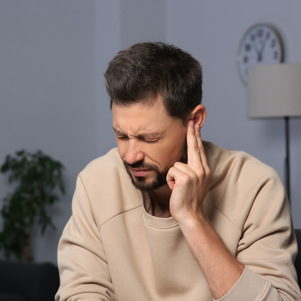 Man suffering from ear pain on in room