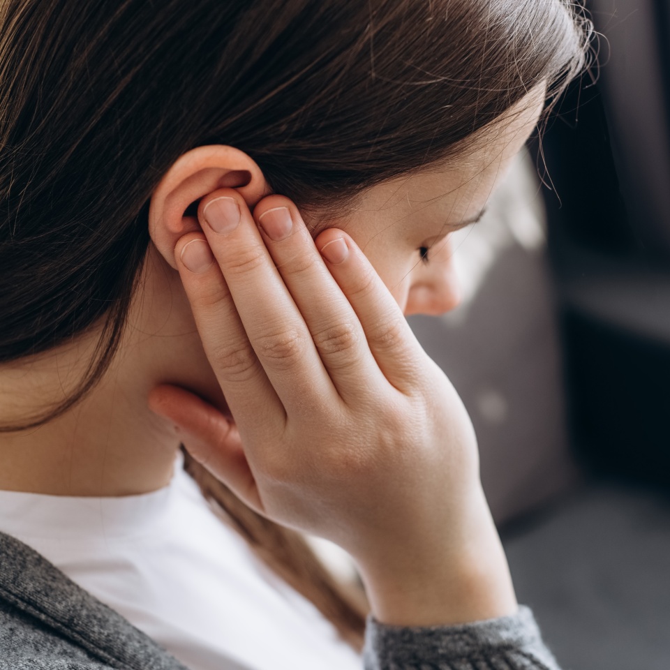 Close up of young brunette female holding painful ear, suddenly feeling strong ache. Unhealthy caucasian woman 20s suffering from painful otitis sitting on couch at home. Health problems concept