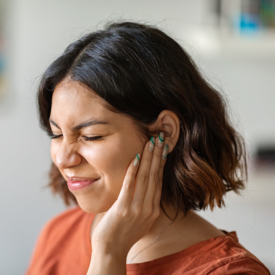 Sick young arab woman having ear pain at home, upset middle eastern female rubbing sore auricle with hand and frowning, suffering from otitis and acute ache, closeup shot with copy space