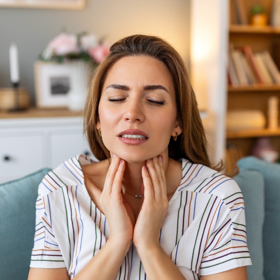 Close up of young woman rubbing her inflamed tonsils, tonsilitis problem, cropped. Woman with thyroid gland problem, touching her neck, girl has a sore throat