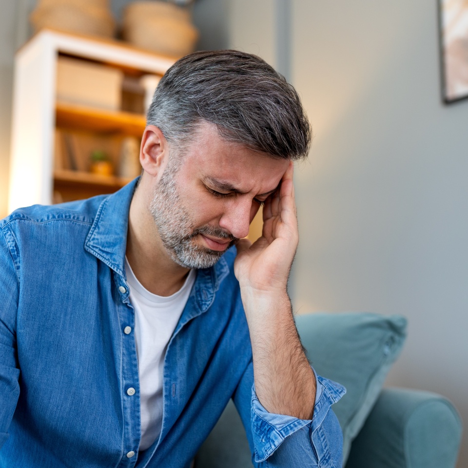 Closeup of man suffering from headache at home, touching his temples, copy space, blurred background. Migraine, headache, stress, tension problem, hangover concept