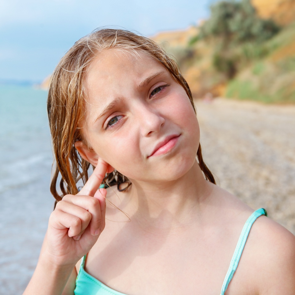 The child got water in his ear while swimming in the sea. The girl cleans her ear from water.