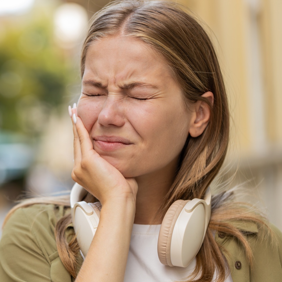 Portrait of young Caucasian woman standing outdoors feeling toothache bad unpleasant symptoms suffering from pain holding hand on cheek jaw damaged dental nerve needs medical help. Girl on city street