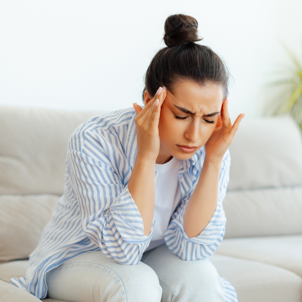 Stress, headache, illness. Upset mixed race woman sitting on a sofa in living room with eyes closed, suffering headache, vertigo, migraine, having cramp in a templess, need treatment and rest