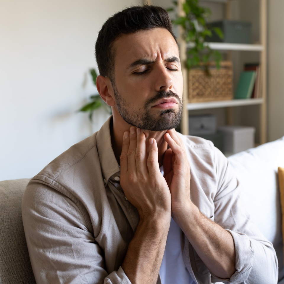 Man suffering from sore throat touching neck feeling pain. Copy space. Health and medical concepts.