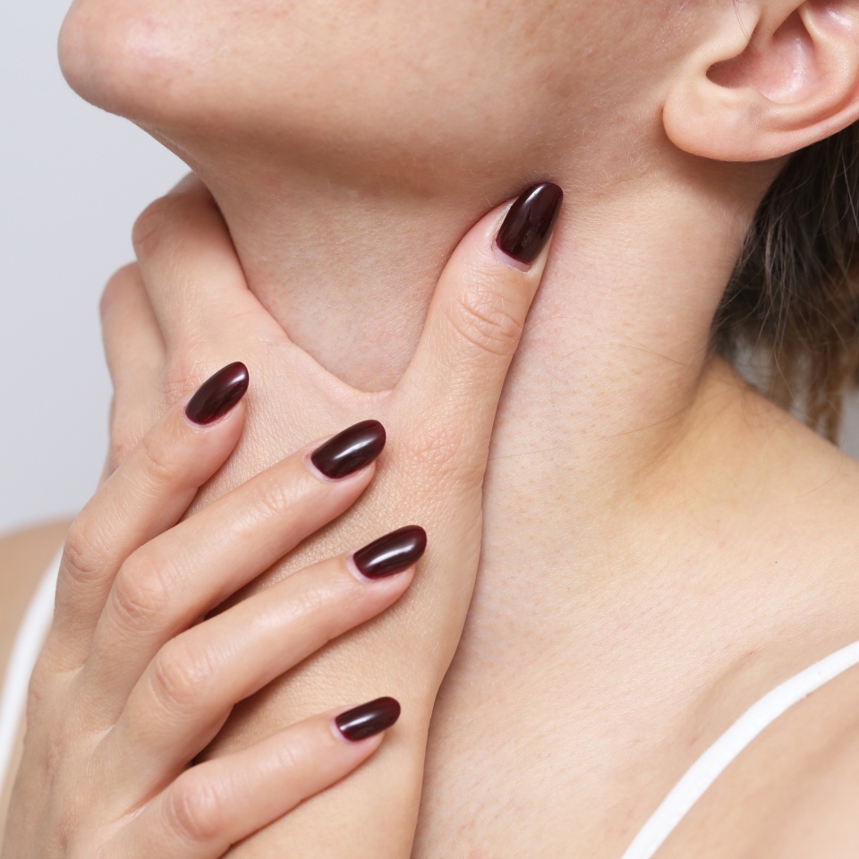Woman holding her throat in discomfort. Experiencing a sore throat due to a cold. Tonsils pain problem. Common symptom of seasonal illness or infection.