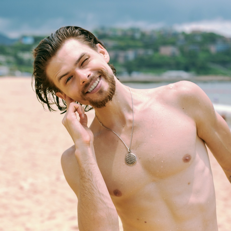 Young handsome guy with a beard on the beach shakes water out of his ear.