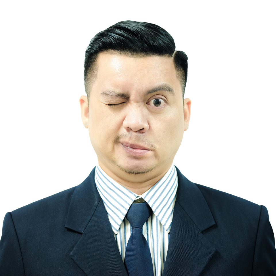 Man in a suit and tie making a facial expression with one eye closed and lips pursed, standing against a white background.