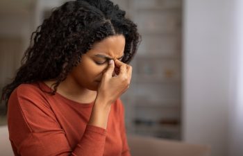 Young black woman feeling sinus pain, pressing on the bridge of her nose, sick african american woman closing eyes and frowning, showing signs of discomfort or headache at home, closeup