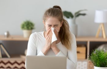 Ill young woman caught cold sneezing in tissue at home or in office, sick allergic girl blowing wiping running nose got flu rhinitis sinusitis coughing, having seasonal allergy symptoms at workplace